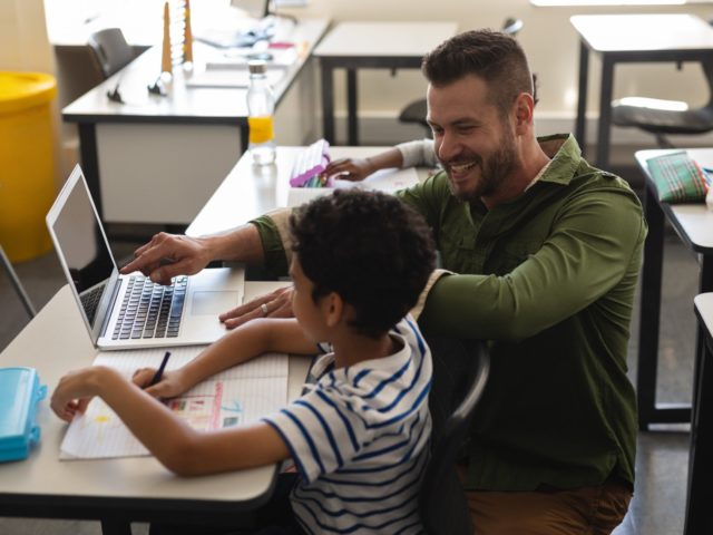 Young school teacher helping boy with study on laptop in
