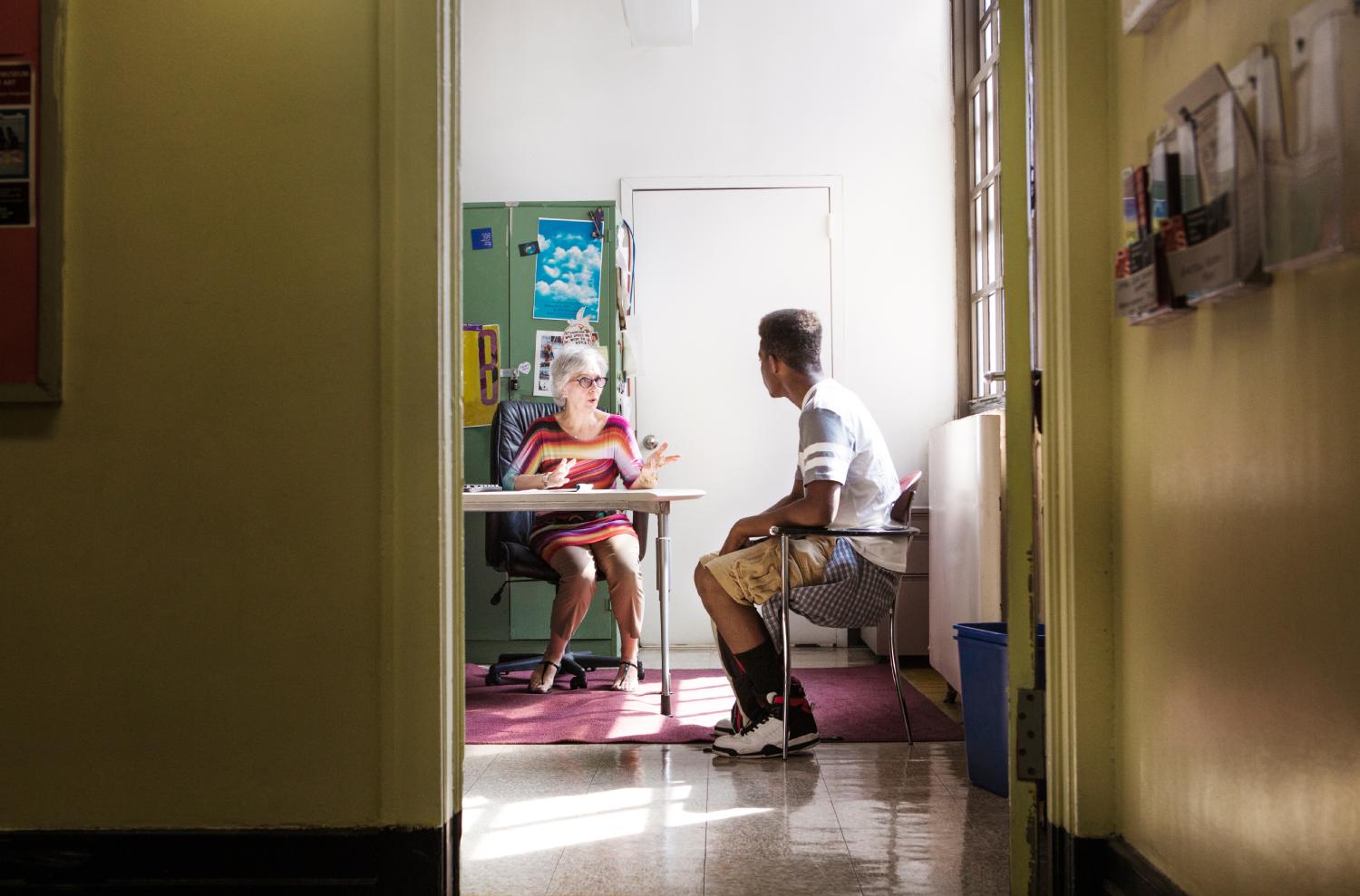 Principal talking with teenage boy while sitting in office