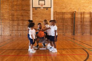 Schoolkids and basketball coach forming hand stack at basketball court in school